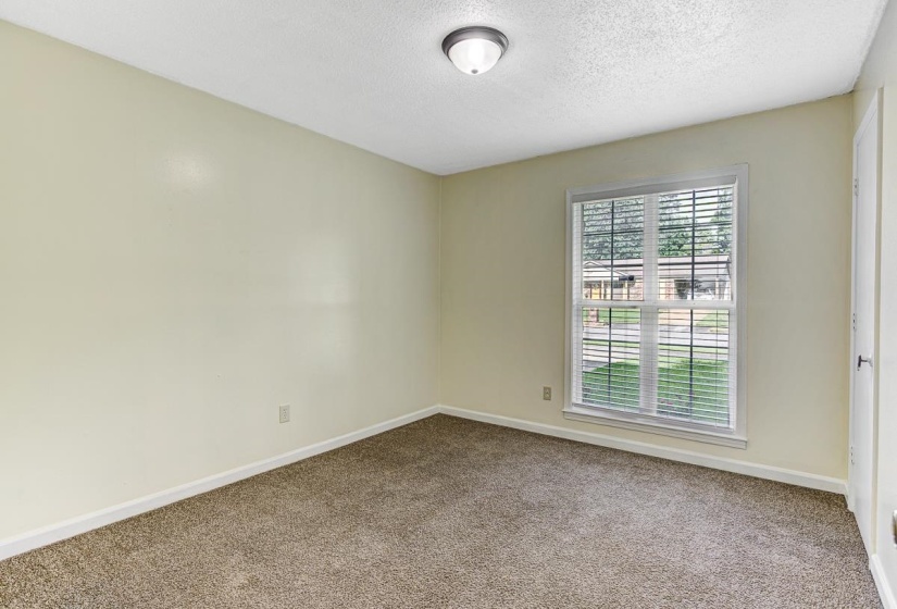 Spacious room featuring neutral wall paint, textured carpeting, a double window with blinds, and a flush mount ceiling light