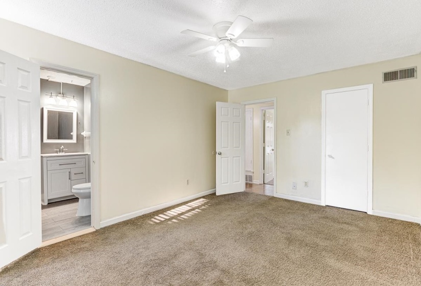 Carpeted room featuring a ceiling fan with integrated lighting, a neutral wall color, and a white door leading to a bathroom