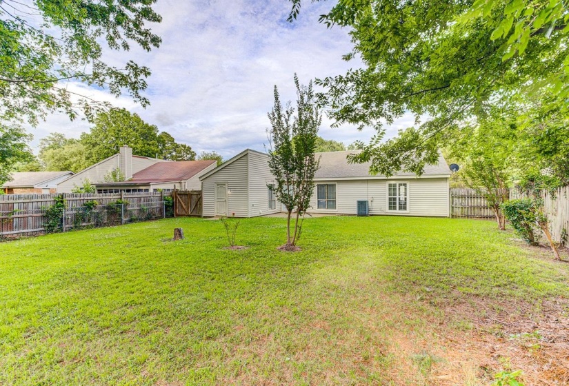 Expansive fenced backyard featuring a manicured lawn, established perimeter trees, and a beige siding exterior with multiple windows