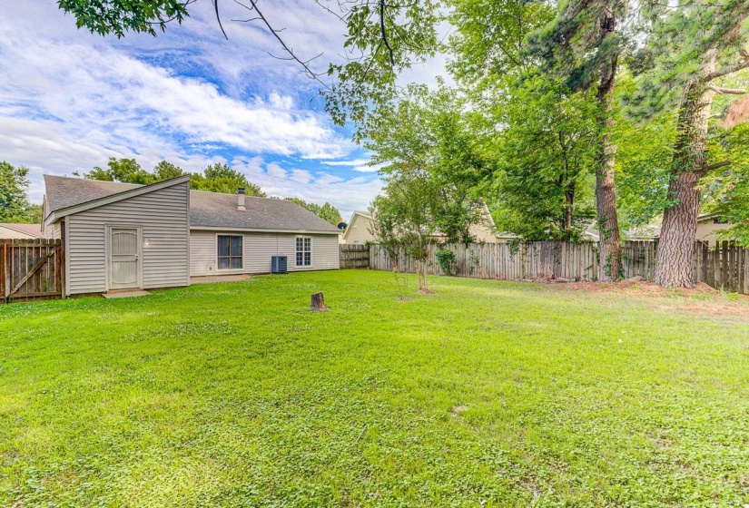 Spacious backyard with expansive lawn, mature perimeter trees, and a wooden privacy fence