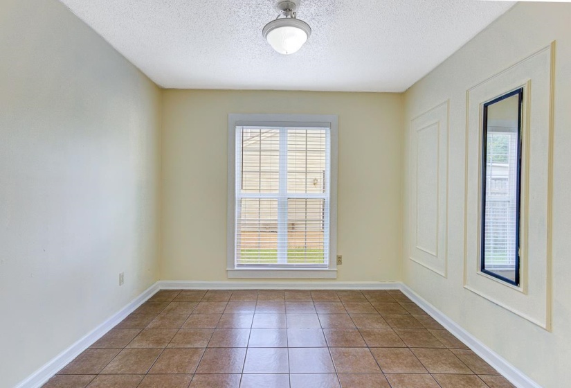 Interior room featuring neutral wall tones, tile flooring, a window with horizontal blinds, decorative wall paneling, and a ceiling-mounted light fixture