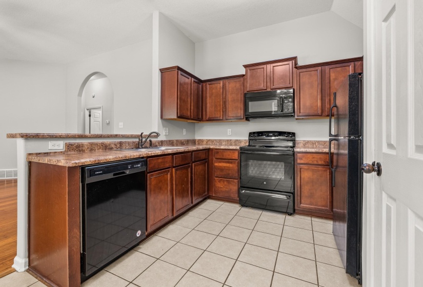 Kitchen featuring wood-finish cabinetry, black appliances, a double-basin sink, and tile flooring