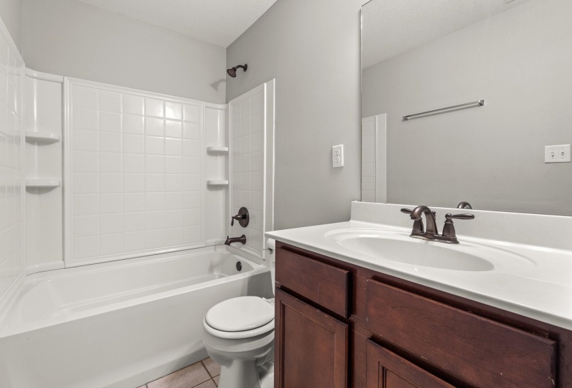Bathroom featuring a white tub/shower combination with integrated shelving, dark bronze fixtures, a dark wood-finish vanity, white countertop with an integrated sink, and a large wall mirror