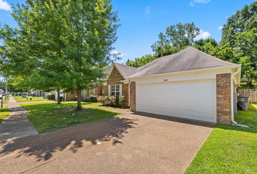 Brick exterior featuring a two-car garage with a white panel door, a concrete driveway, and a sidewalk