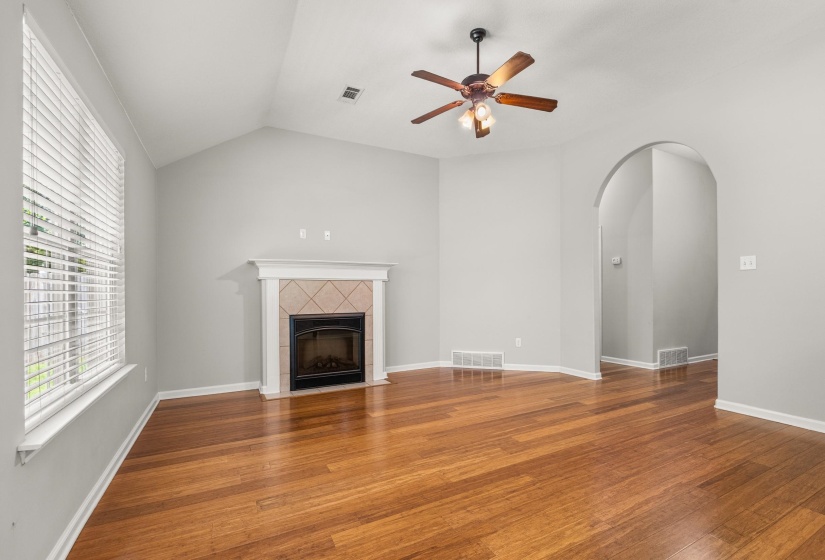 Spacious living area featuring wood-finish flooring, a fireplace with a tile surround, and an arched doorway