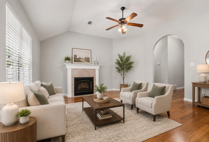Vaulted ceiling living area featuring a fireplace with tiled surround, wood-finish flooring, a ceiling fan, and an arched entry