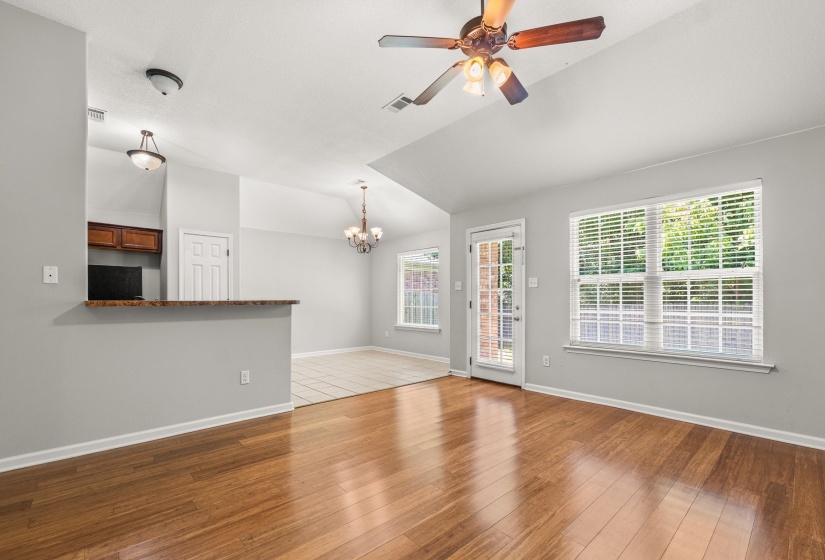 Spacious living area featuring wood-finish flooring, vaulted ceilings, and a ceiling fan with integrated lighting