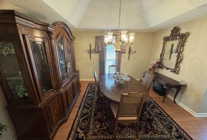 Dining area featuring wood-finish flooring, a tray ceiling, and a multi-arm chandelier with frosted glass shades