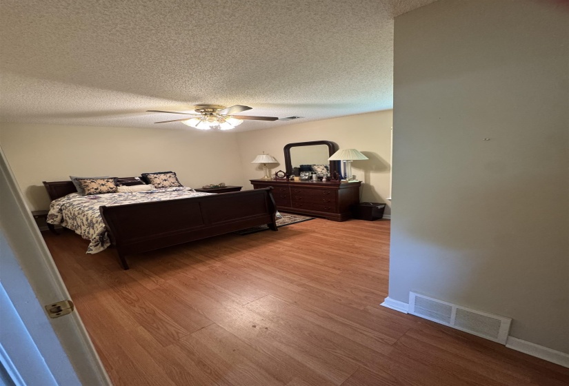 Spacious room featuring wood-finish flooring, a textured ceiling, and a ceiling fan with integrated lighting