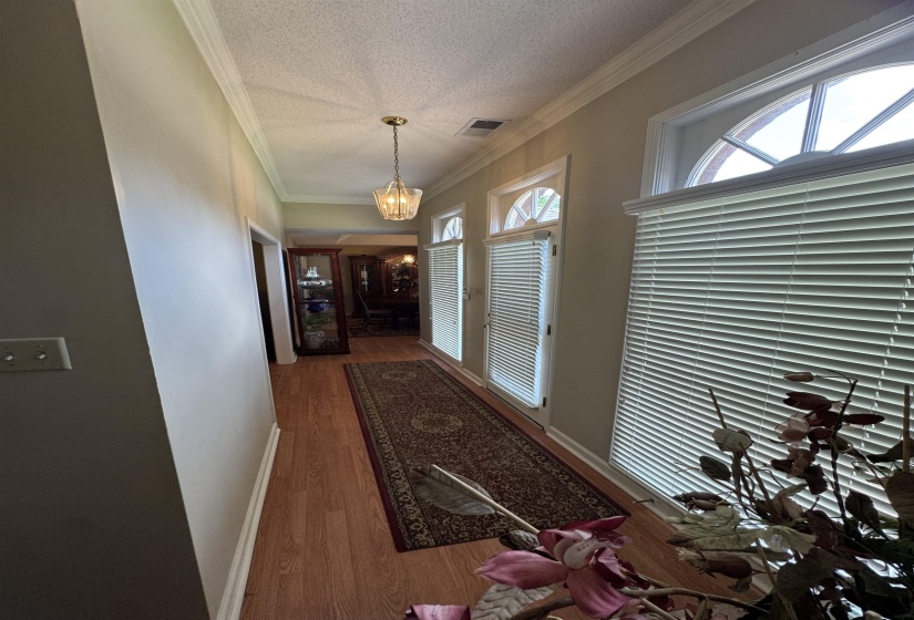 Hallway featuring wood-finish flooring, a decorative chandelier, multiple arched transom windows, horizontal blinds, and crown molding