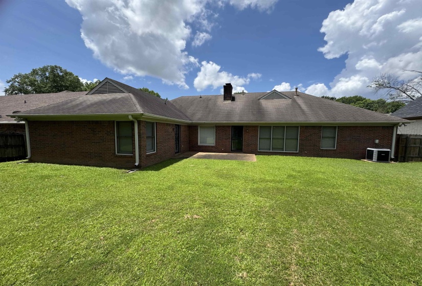 Expansive rear yard featuring a brick facade, gabled rooflines, multiple windows, a concrete patio, and a visible HVAC unit