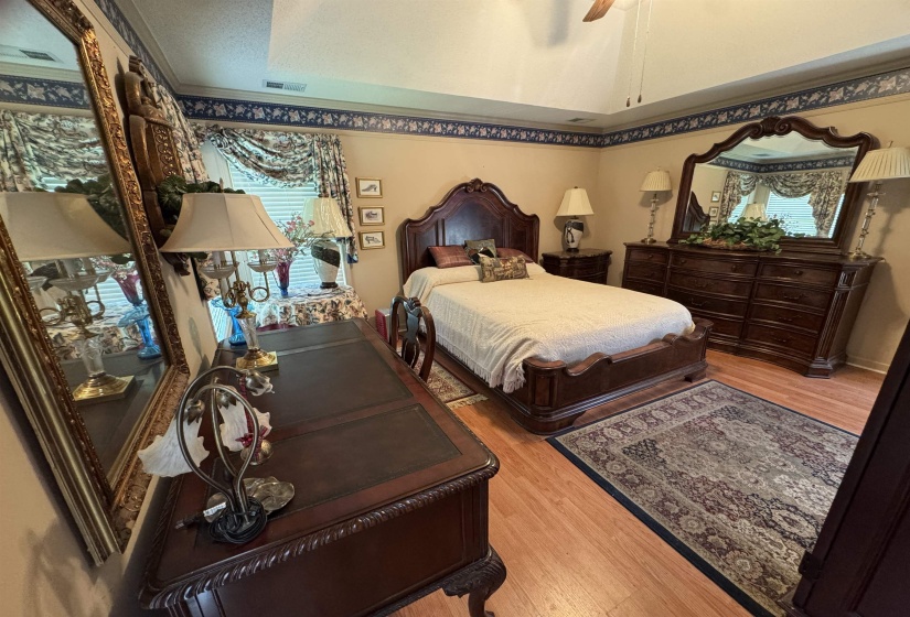 Room featuring wood-finish flooring, a tray ceiling with a ceiling fan, and a window with valance treatments