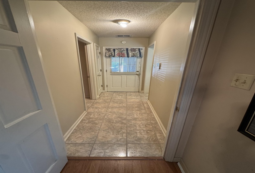 Hallway featuring light-toned square tile flooring extending to a white paneled exterior door with an overhead window