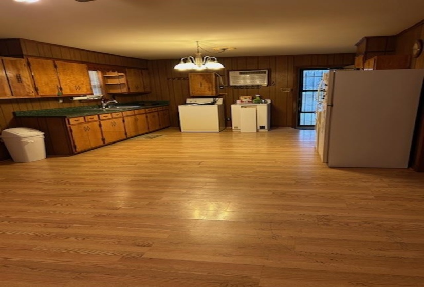 Kitchen featuring dark countertops, freestanding refrigerator, brown cabinetry, wood walls, and washer / clothes dryer