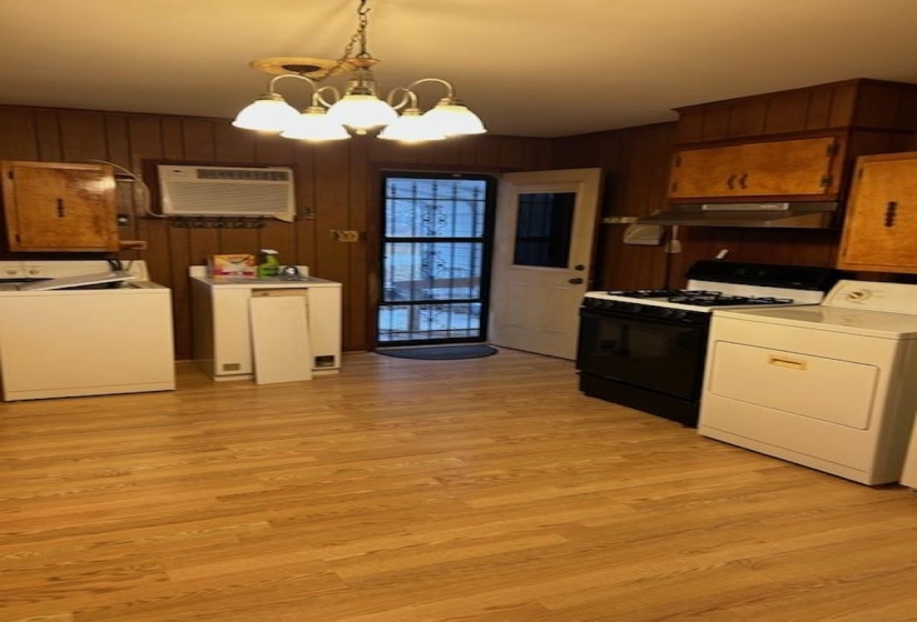 Kitchen featuring gas stove, a chandelier, pendant lighting, wooden walls, and light wood finished floors