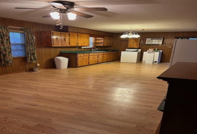 Kitchen with dark countertops, brown cabinets, white appliances, a ceiling fan, and wood walls