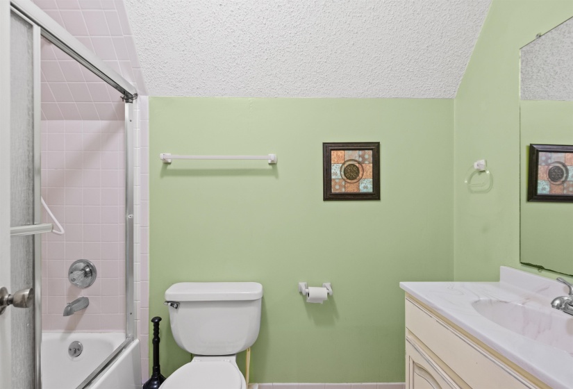 Bathroom featuring a tub/shower combination with pink wall tile, a white vanity with an integrated sink and light-colored countertop, and a white toilet
