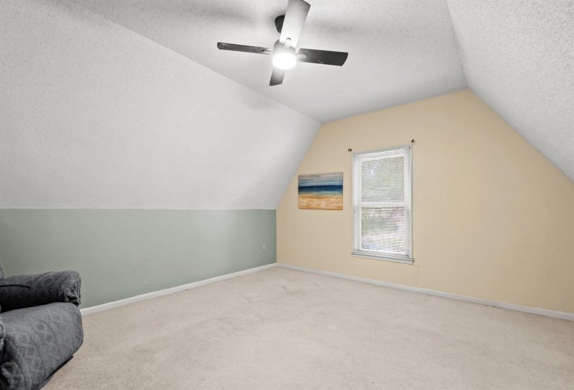 Spacious room featuring vaulted ceilings, a ceiling fan with integrated lighting, and neutral-toned carpeting