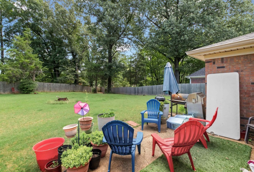 Expansive backyard featuring a privacy fence, mature trees, and a concrete patio