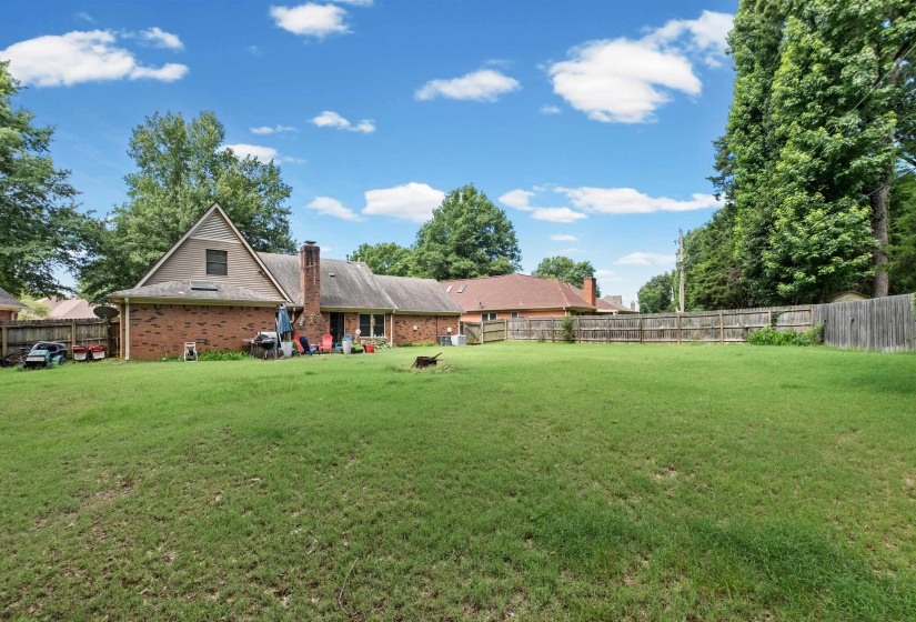 Expansive grassy lawn with surrounding mature trees and a wood privacy fence