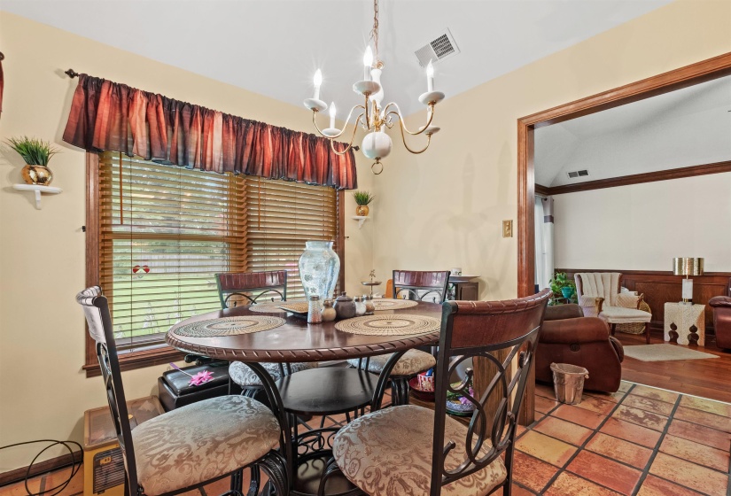 Dining area featuring a central chandelier, a large window with horizontal blinds, and a tiled floor