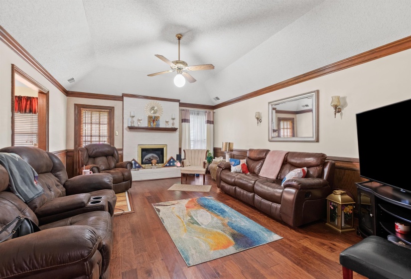 Spacious living area featuring wood-finish flooring, wainscoting, and a vaulted ceiling with a ceiling fan