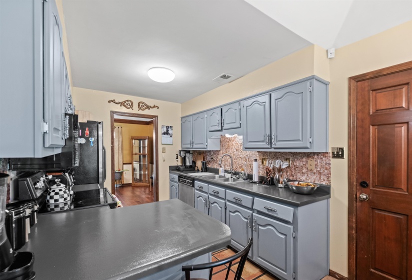 Kitchen featuring gray cabinetry, dark countertops, a mosaic tile backsplash, stainless steel sink, and durable tile flooring