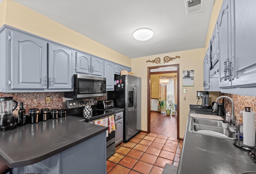 Kitchen featuring slate blue cabinetry, stainless steel appliances, terracotta tile flooring, and dark countertops