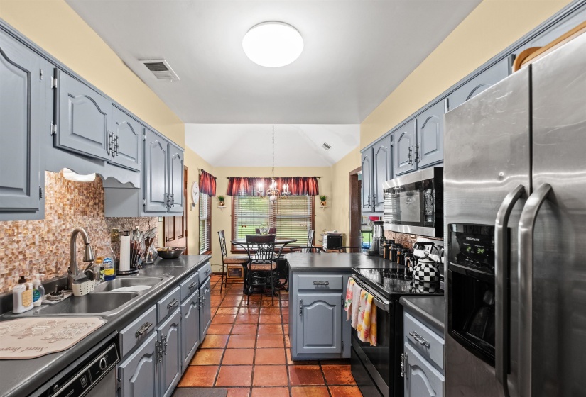 Galley kitchen featuring terracotta tile flooring, gray cabinetry, dark countertops, and a tiled backsplash