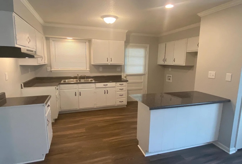 Kitchen featuring white cabinetry, dark stone countertops, wood-finish flooring, a stainless steel sink with a chrome faucet, and a peninsula with a dark stone counter