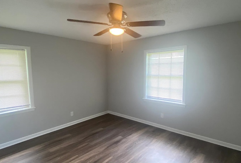 Room featuring wood-finish flooring, two windows with blinds, a ceiling fan with integrated lighting, and light gray wall paint