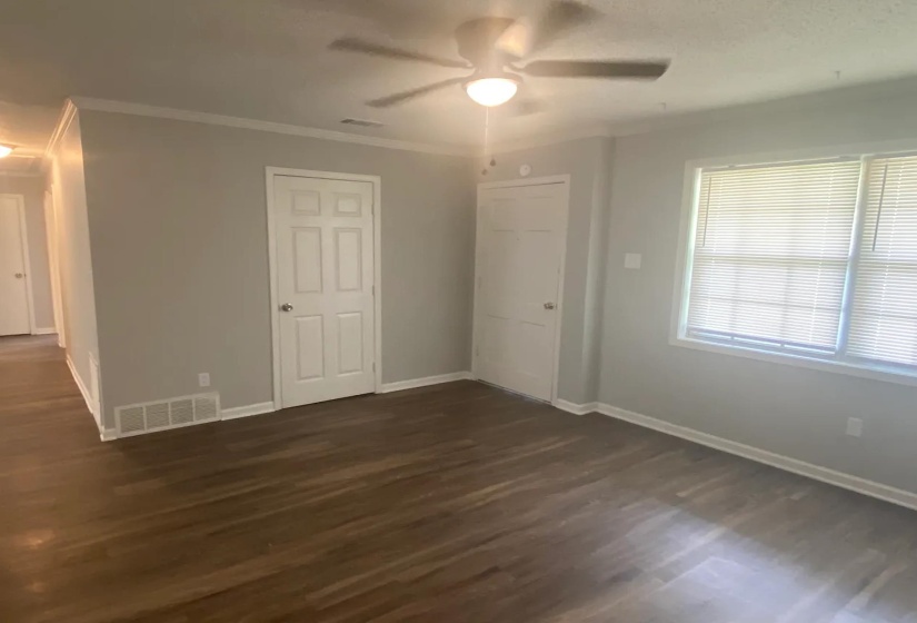 Spacious room featuring wood-finish flooring, light gray walls, and crown molding