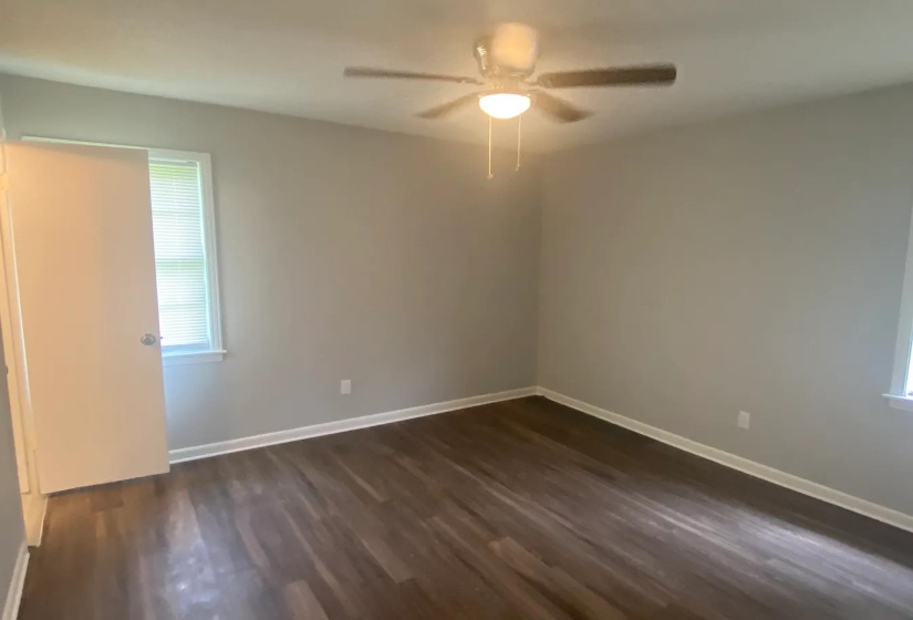 Neutral-toned room featuring rich wood-finish flooring, a ceiling fan with integrated lighting, and white baseboards