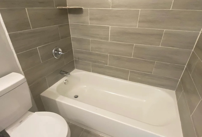 Bathtub with chrome fixtures, surrounded by horizontal tile work extending to a built-in shelf