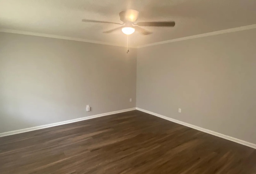Spacious room featuring wood-finish flooring, light gray wall paint, white crown molding, white baseboards, and a ceiling fan with integrated lighting