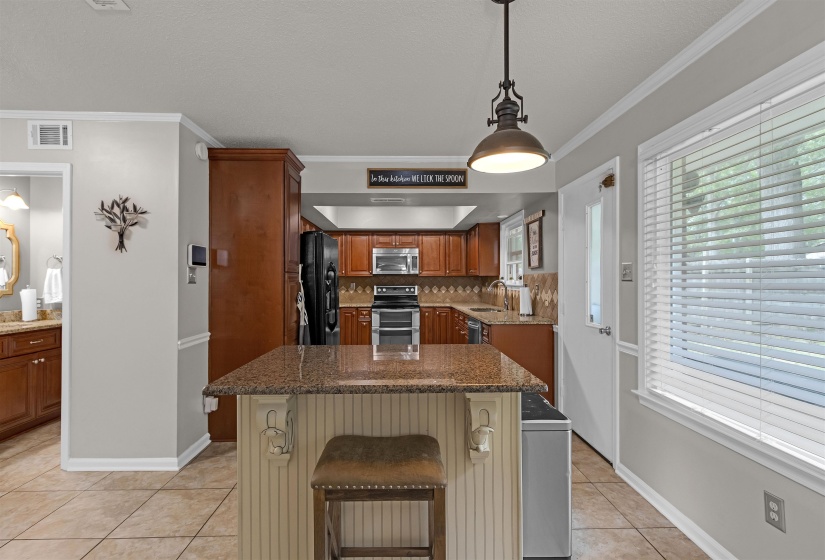 Kitchen featuring a central island with a granite countertop and beadboard paneling, tiled flooring, wood cabinetry, and stainless steel appliances