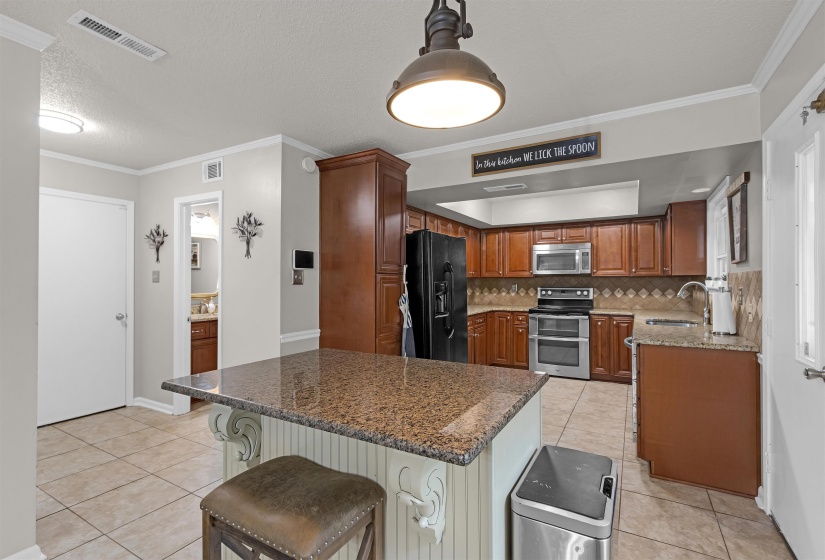 Kitchen featuring a central island with a granite countertop, wood-finish cabinetry, stainless steel appliances, and tile flooring