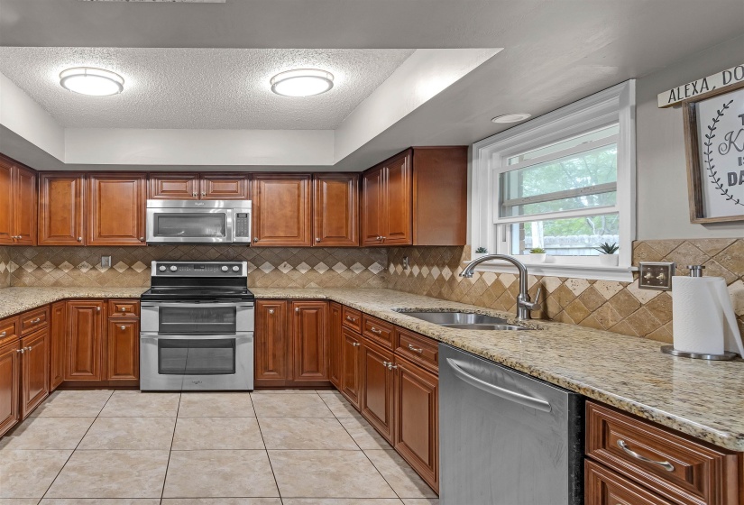 U-shaped kitchen featuring wood cabinetry, stainless steel appliances, speckled countertops, a tile backsplash, and ceramic tile flooring
