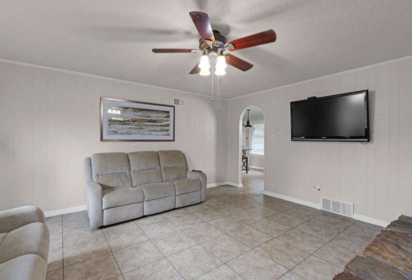 Spacious room featuring tile flooring, light-toned vertical paneling, and a ceiling fan with integrated lighting