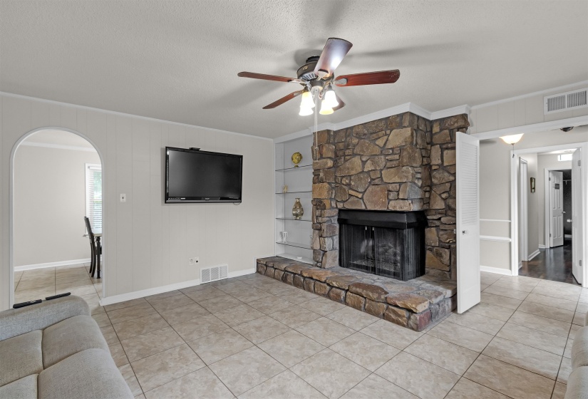 Living area featuring a stone fireplace with hearth, tile flooring, and ceiling fan