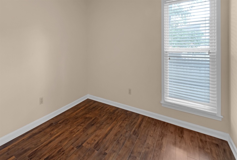 Room featuring wood-finish flooring, neutral wall paint, white baseboards, and a window with white blinds
