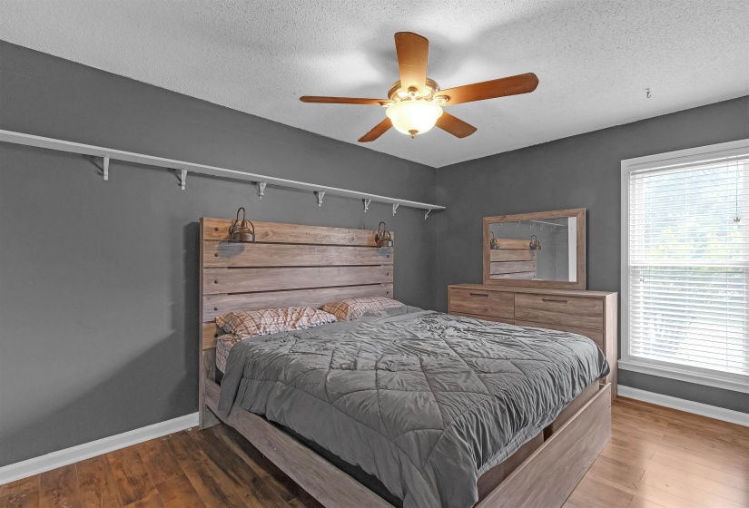 Room featuring wood-finish flooring, a ceiling fan with integrated lighting, and a window with blinds