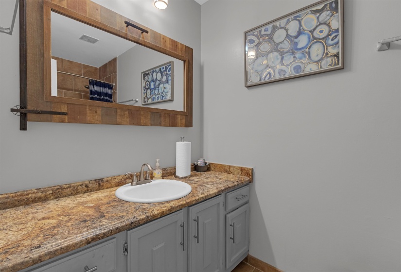 Vanity area featuring a wood-framed mirror, undermount sink, stone-finish countertop, and gray cabinetry