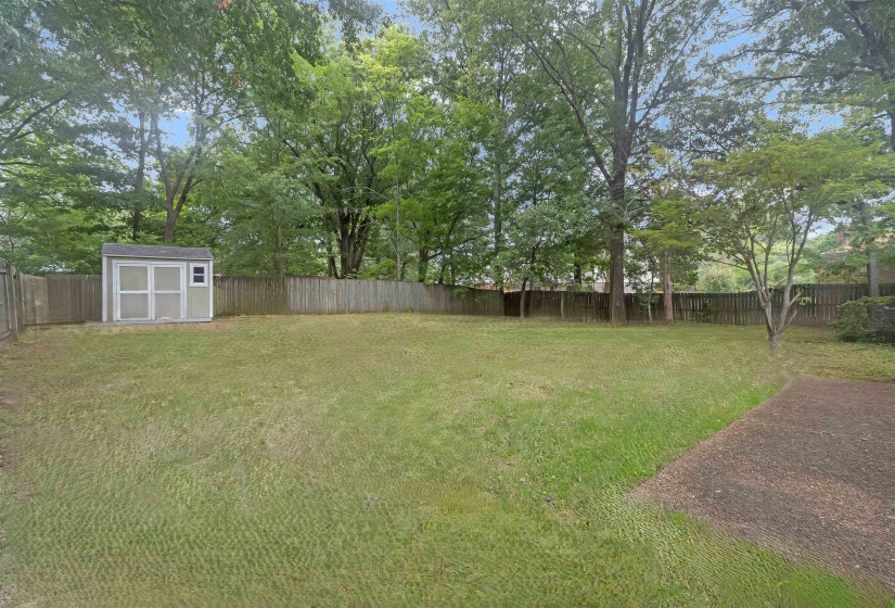 Expansive backyard featuring a privacy fence, mature trees, and a detached storage shed