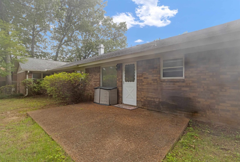 Rear exterior featuring a brick facade, white panel door with glass insert, and a concrete patio