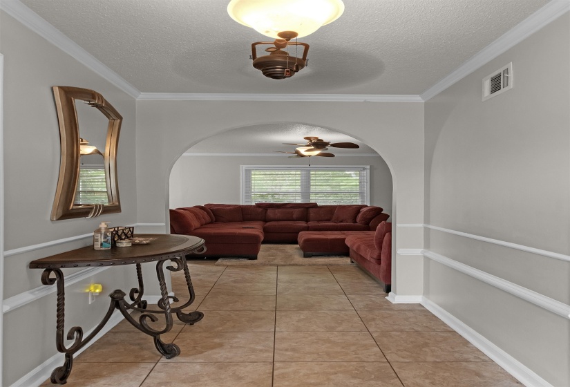 Tiled entryway featuring crown molding, chair rail molding, and an arched doorway leading to a room with windows and a ceiling fan