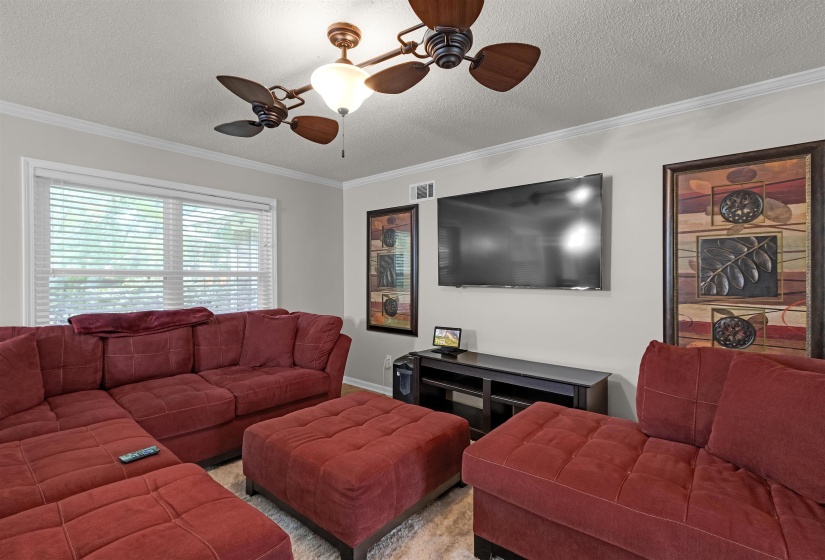 Living area featuring a ceiling-mounted fan with integrated lighting, crown molding, wall-mounted television, and wood-finish flooring