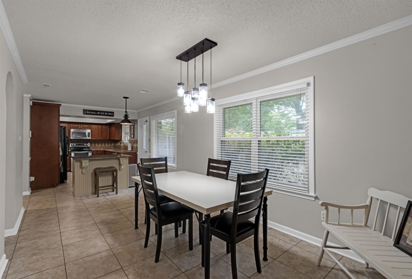 Open-concept dining area featuring tile flooring, crown molding, and a modern linear chandelier