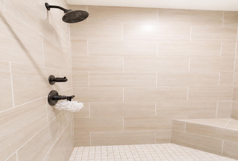 Walk-in shower featuring large format tile walls, mosaic tile flooring, a built-in shower bench, and oil-rubbed bronze fixtures