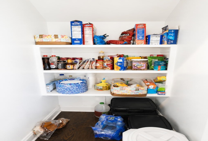 Pantry featuring three white built-in shelves, white walls, and dark wood-finish flooring